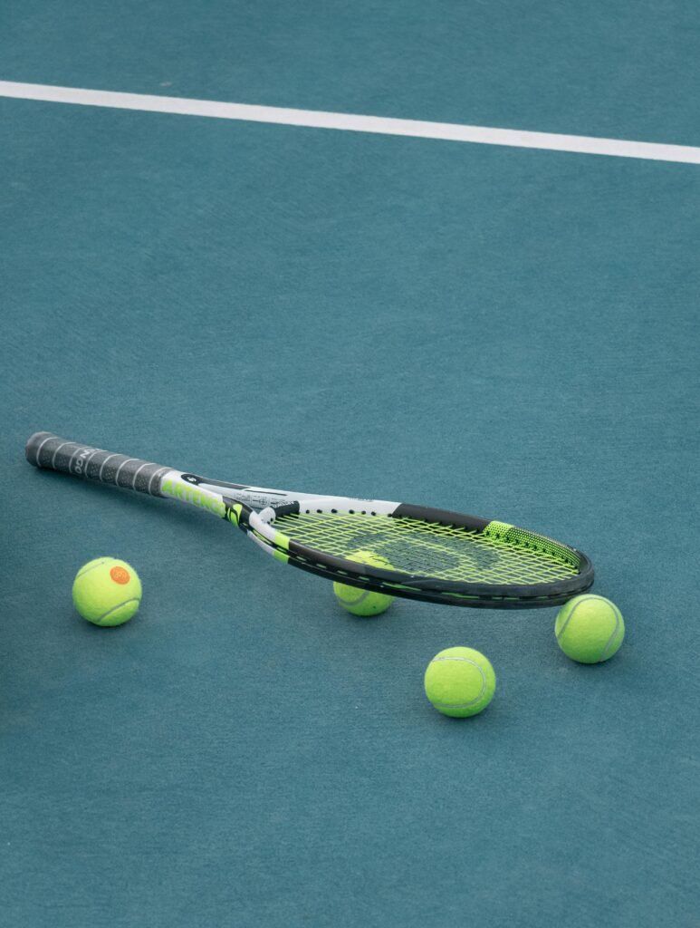 Tennis racket and balls on a blue court surface under day light.